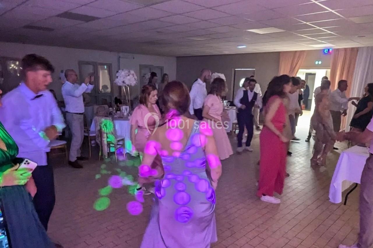 Personnes dansant dans une salle éclairée par des lumières colorées, lors d'un événement festif en intérieur.