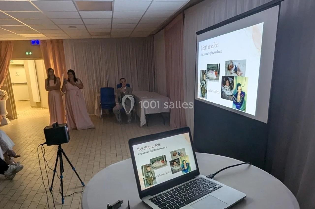 Projection d'un diaporama sur un écran dans une salle, avec des personnes assises et debout en arrière-plan.