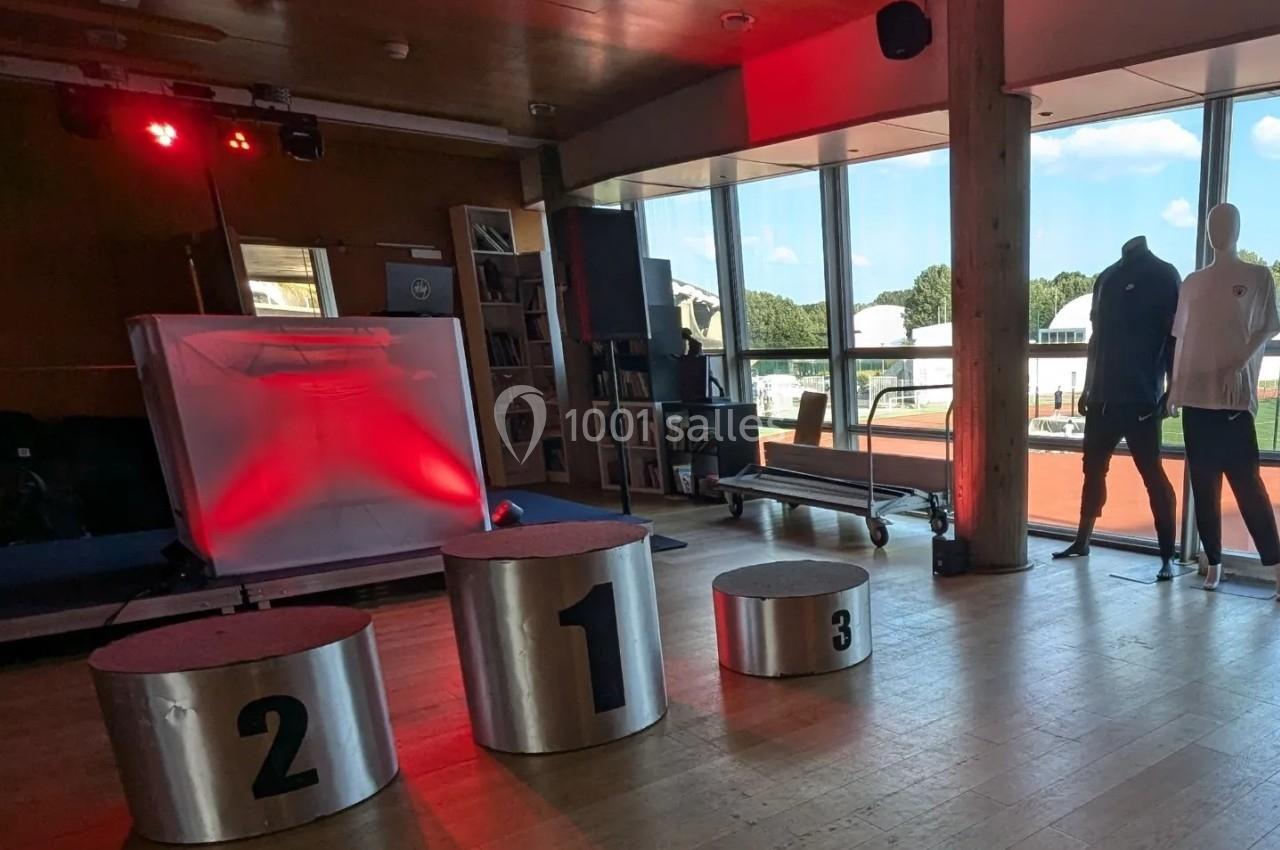 Salle lumineuse avec podiums numérotés, éclairage rouge, mannequins et vue sur l'extérieur à travers de grandes baies…