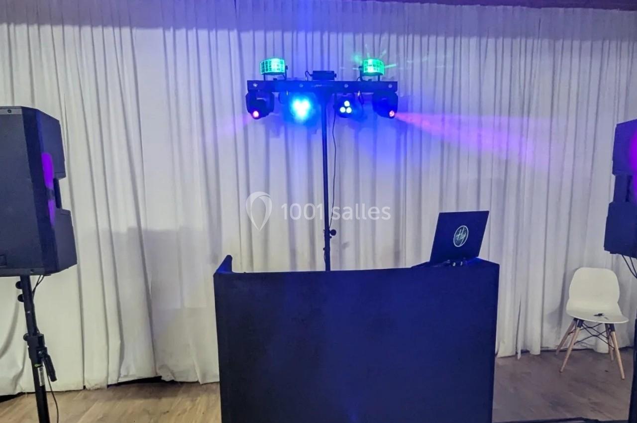 Installation de DJ avec table noire, éclairages colorés et enceintes devant un rideau blanc.