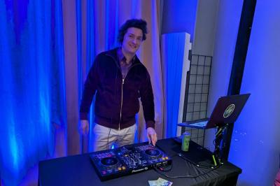 Un homme s'exprime au micro devant un public rassemblé dans une cour extérieure entourée de végétation.