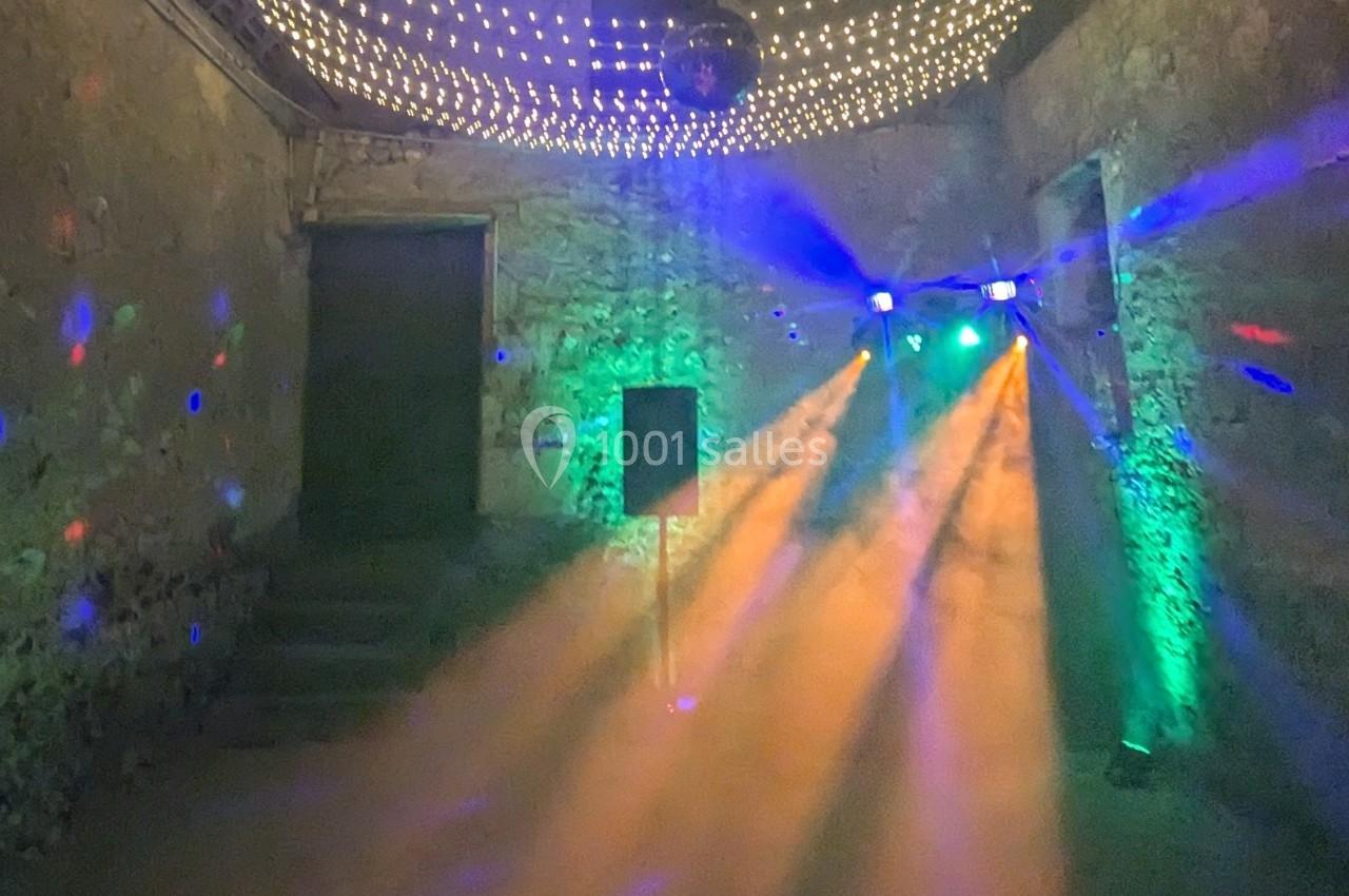 Salle en pierre avec éclairage coloré, projecteurs et fumée créant une ambiance festive.