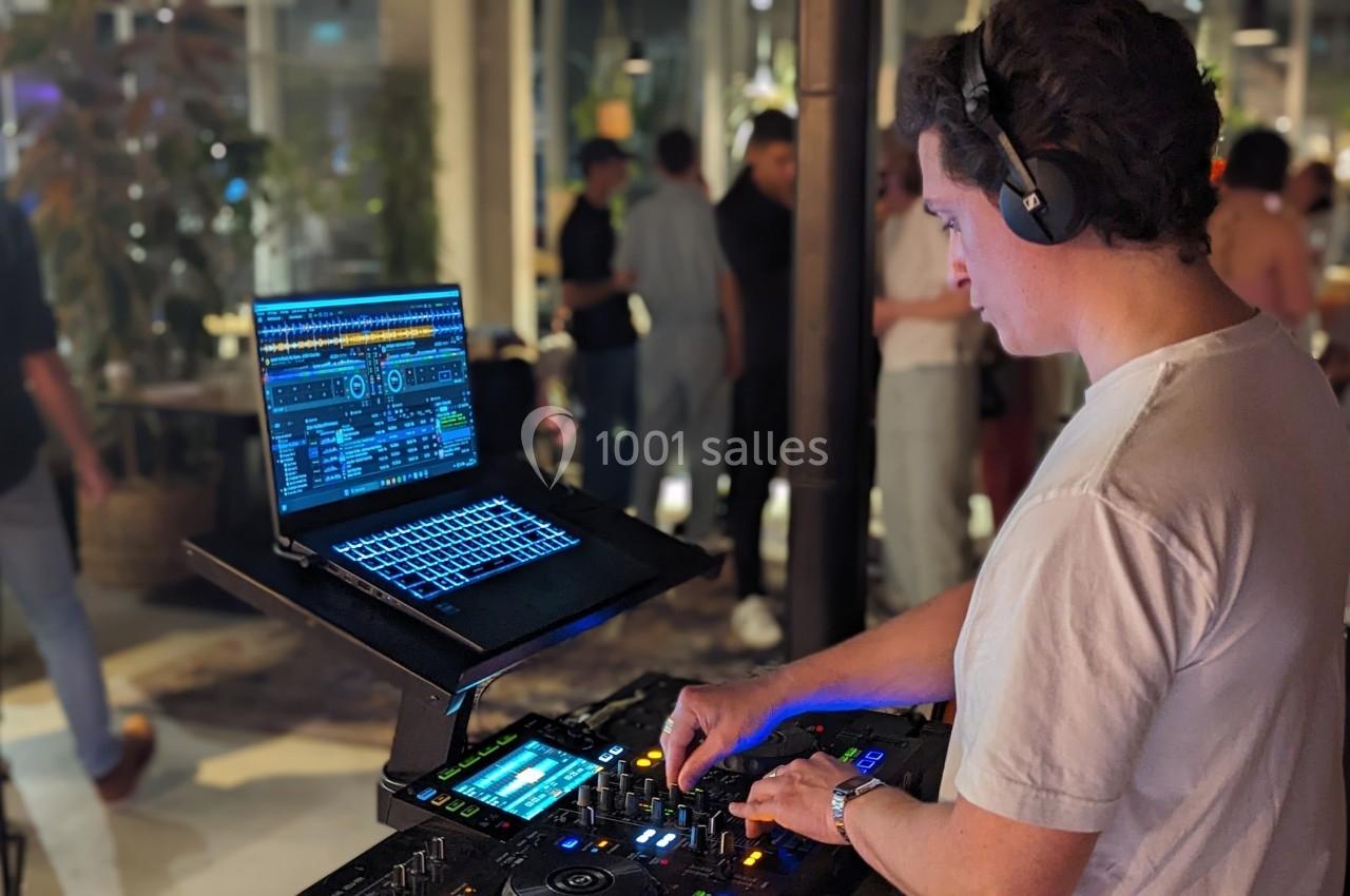 Un DJ mixe de la musique sur une console avec un ordinateur portable, dans un espace intérieur animé.