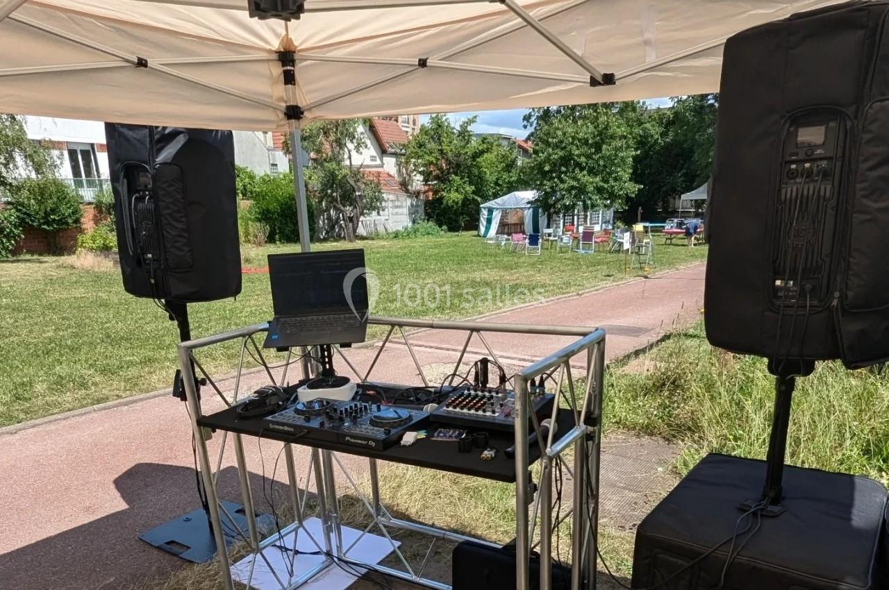 Poste de DJ en plein air sous une tente, avec platines, ordinateur portable et enceintes, dans un cadre verdoyant.