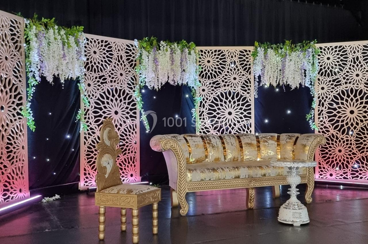 Décor élégant avec un canapé doré, une chaise assortie et des panneaux ajourés ornés de fleurs suspendues.