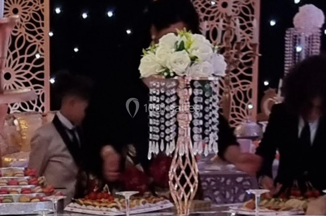 Un centre de table orné de fleurs blanches et de cristaux, entouré de personnes lors d'une réception festive.