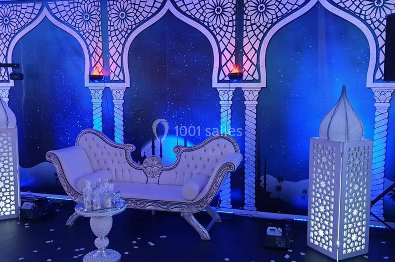 Décor oriental avec canapé blanc sculpté, lanternes ajourées et fond étoilé aux arches ornées de motifs géométriques.