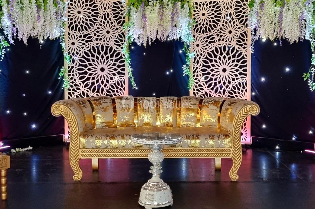 Canapé doré orné de motifs, placé devant un décor floral suspendu et des panneaux décoratifs lumineux.