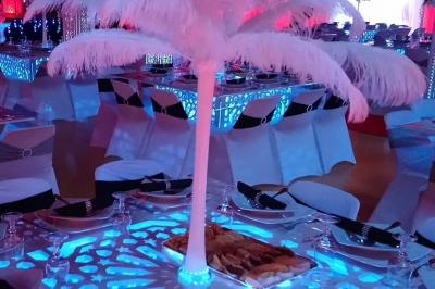Miniature Sable d'Orient Déco Event #24 Salle de réception décorée avec des tables élégantes, nappes blanches, centres de table lumineux et plumes blanches.