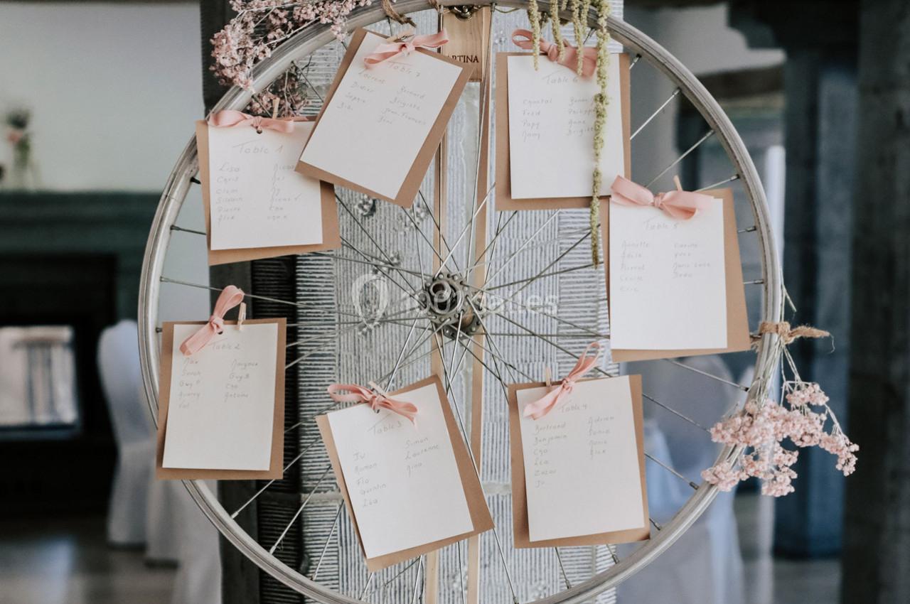 Roue de vélo décorée avec des cartes de table suspendues par des rubans roses et ornée de fleurs séchées.