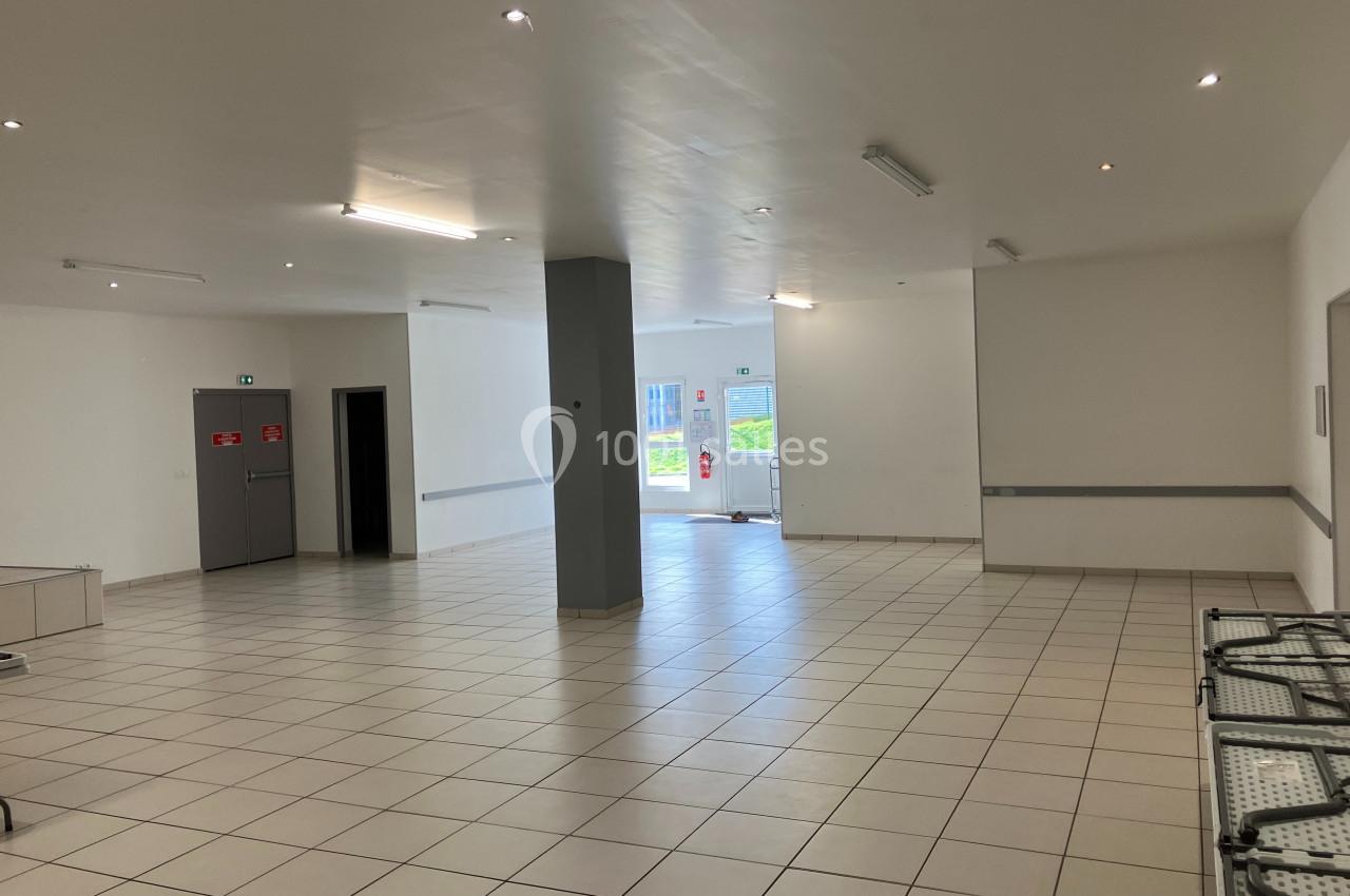 Salle vide avec carrelage clair, murs blancs, éclairage au plafond et porte vitrée donnant sur l'extérieur.