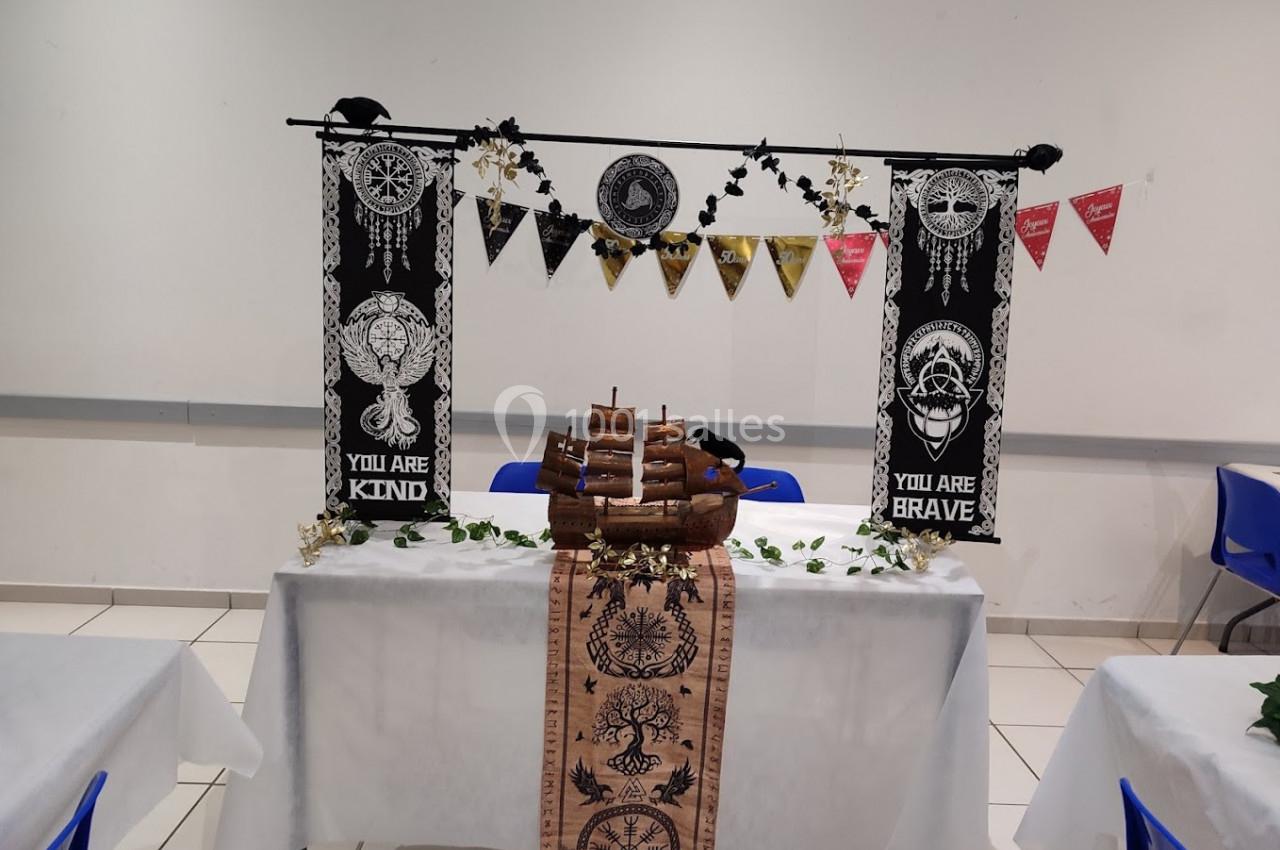 Décoration de table sur le thème marin avec un bateau en bois, bannières et guirlandes dans une salle lumineuse.