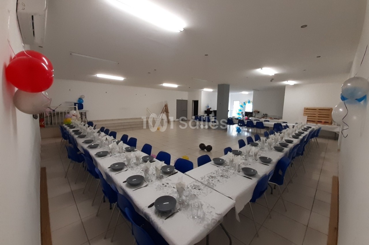 Salle de réception avec deux longues tables dressées en U, décorée de ballons et prête pour un événement.