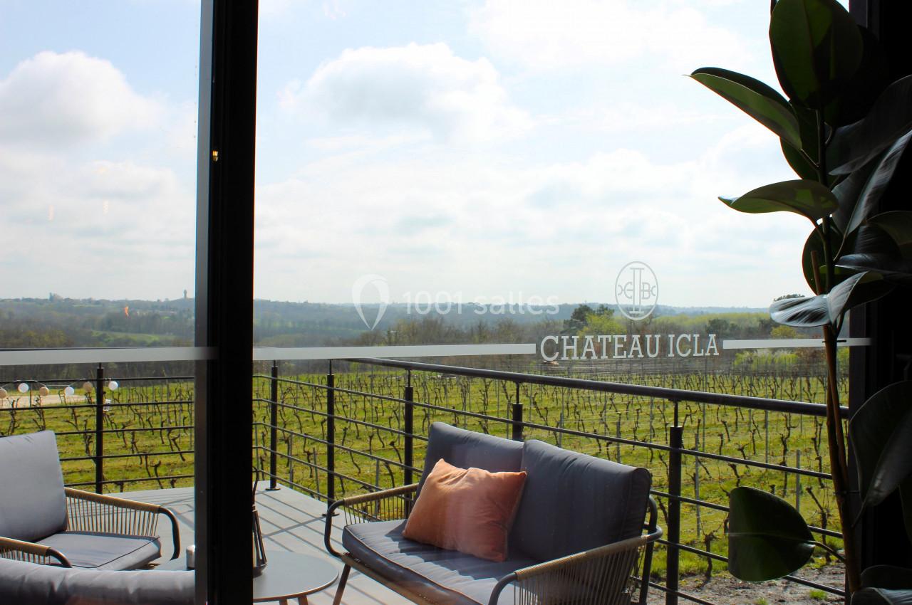 Vue sur des vignes depuis une terrasse avec fauteuils et coussins, encadrée par une baie vitrée et une plante.