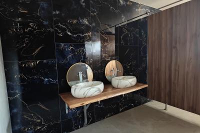 Deux lavabos en marbre blanc avec miroirs ronds sur un plan en bois, devant un mur en carrelage noir marbré.