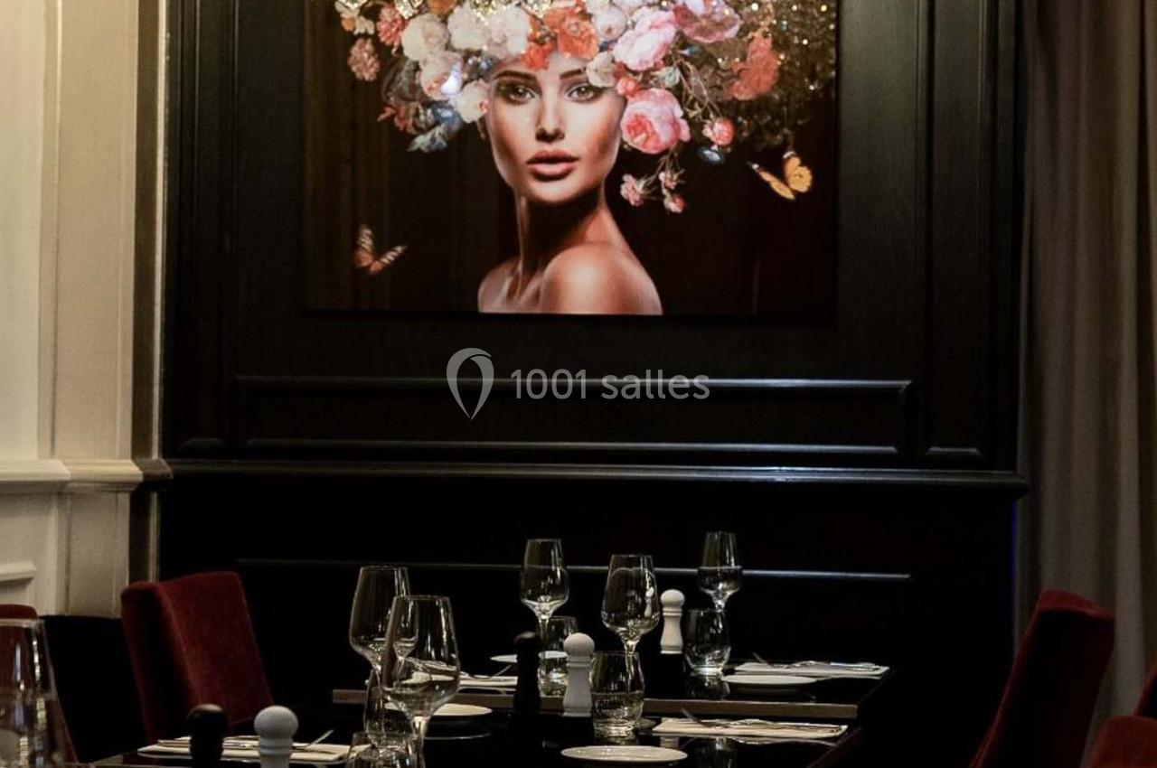 Table dressée dans un restaurant élégant, avec un tableau représentant une femme ornée de fleurs en arrière-plan.
