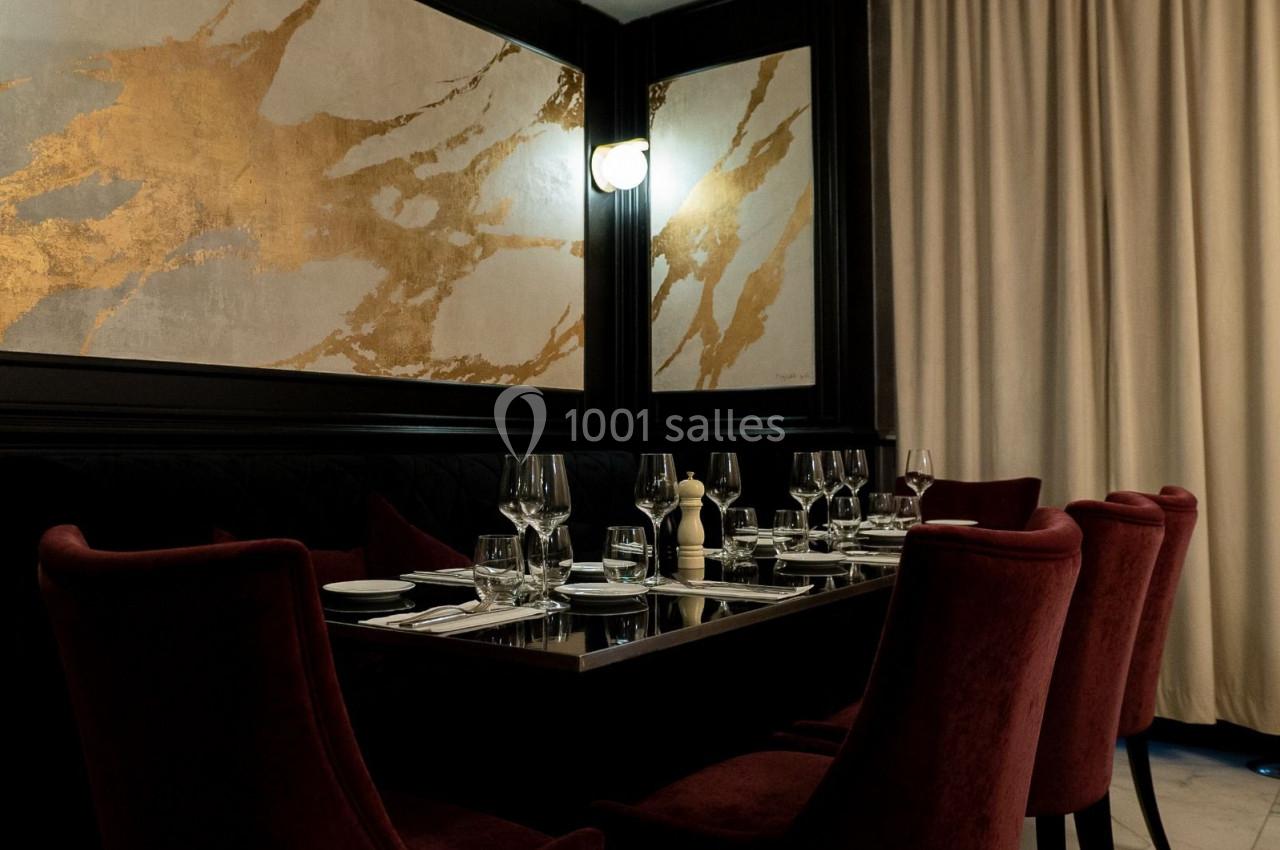 Salle de restaurant élégante avec table dressée, chaises en velours rouge, murs décorés et éclairage tamisé.