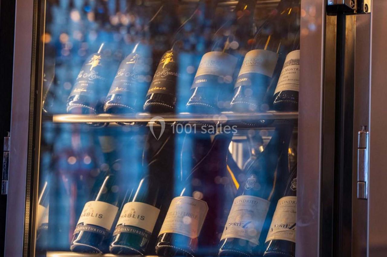 Bouteilles de vin blanc et mousseux rangées inclinées dans une cave à vin réfrigérée avec porte vitrée.