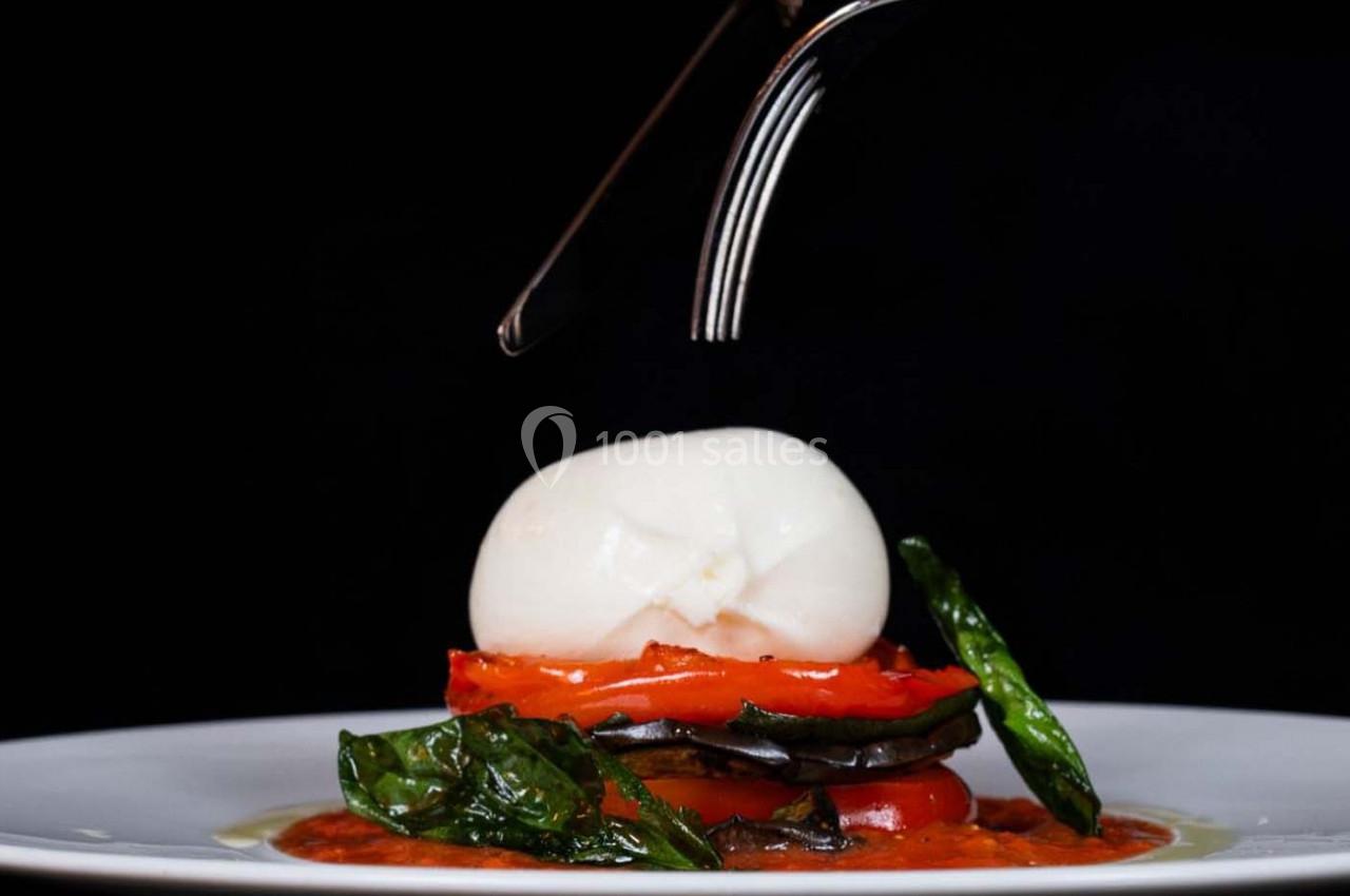 Assiette gourmande avec burrata, légumes grillés, sauce tomate et feuilles de basilic, sur fond noir.