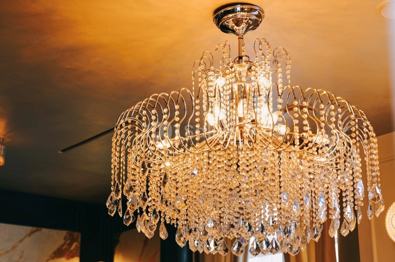 Lustre en cristal suspendu, éclairé, avec des pampilles étincelantes dans une pièce au plafond doré.