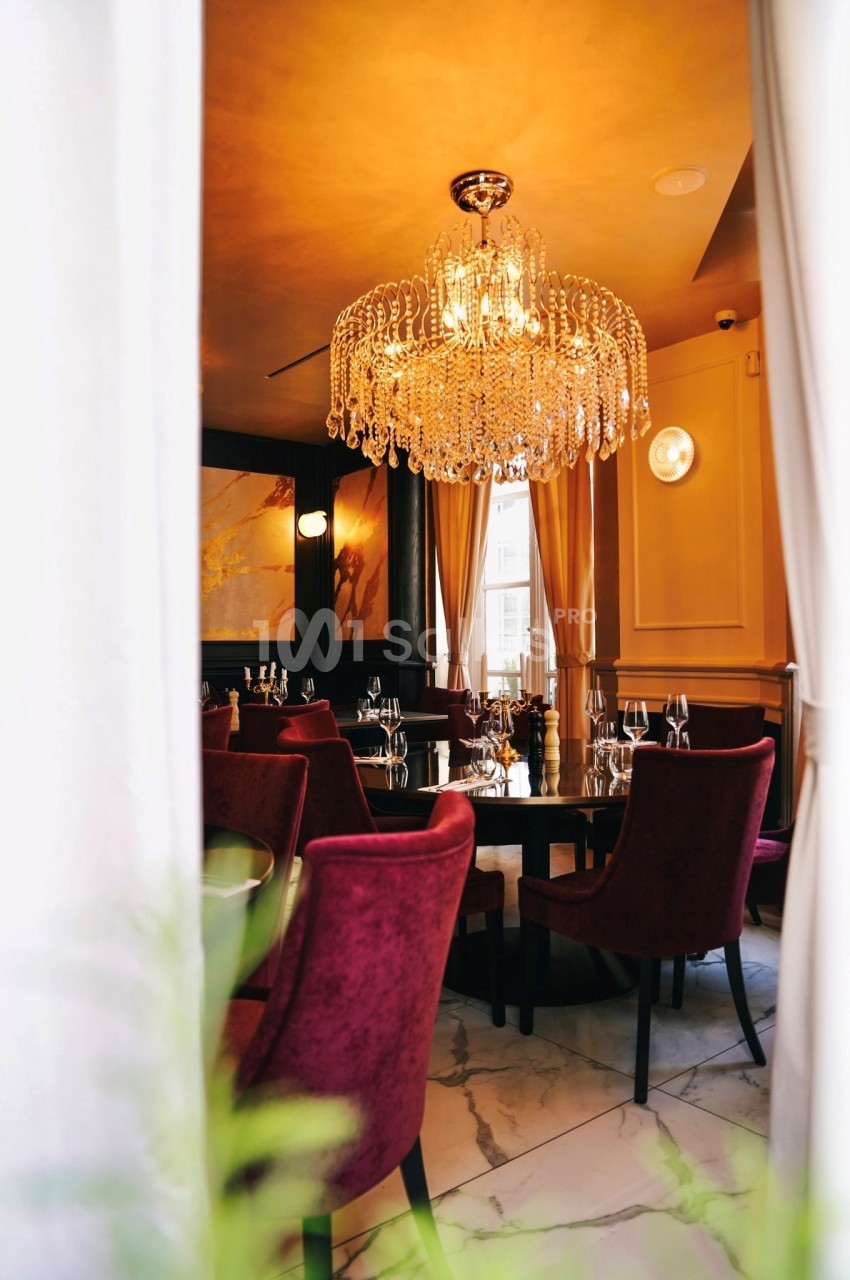 Salle de restaurant élégante avec chaises en velours rouge, table dressée et grand lustre en cristal suspendu.