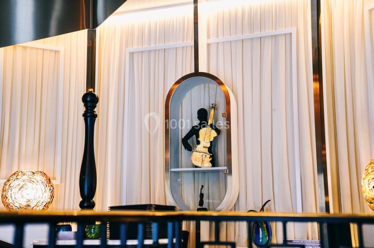 Statue noire d'un musicien jouant du violon, exposée dans une niche éclairée devant un rideau beige.
