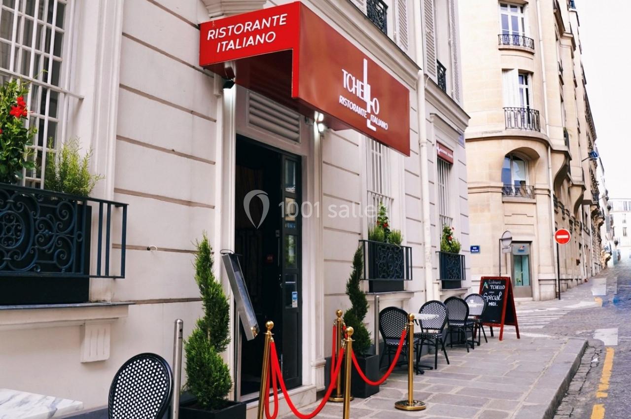Façade d'un restaurant italien avec terrasse, enseigne rouge et décoration de plantes en pots sur un trottoir pavé.
