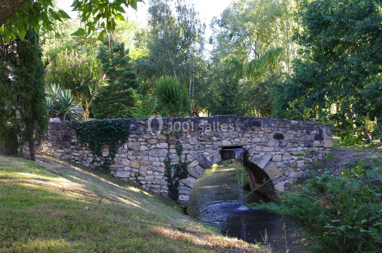 Pont en pierre ancienne enjambant un petit cours d'eau entouré de végétation verdoyante.