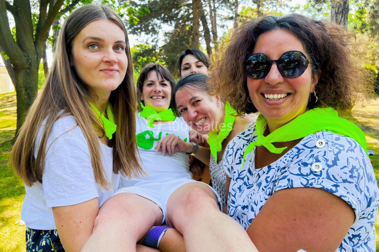 Cinq femmes souriantes portant des foulards verts, réunies dans un parc ensoleillé.