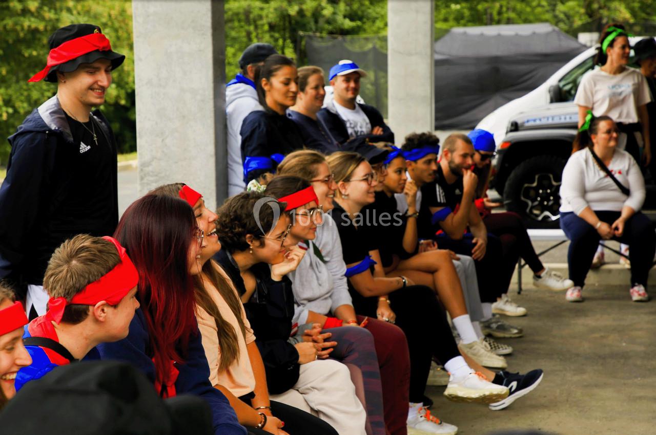 Un groupe de personnes assises sous un abri, portant des bandeaux colorés, lors d'une activité en plein air.