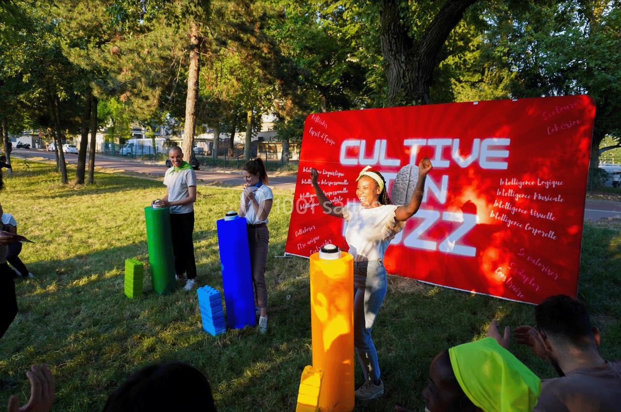 Des personnes participent à une activité en plein air devant une banderole rouge avec l'inscription ’Cultive ton buzz’.