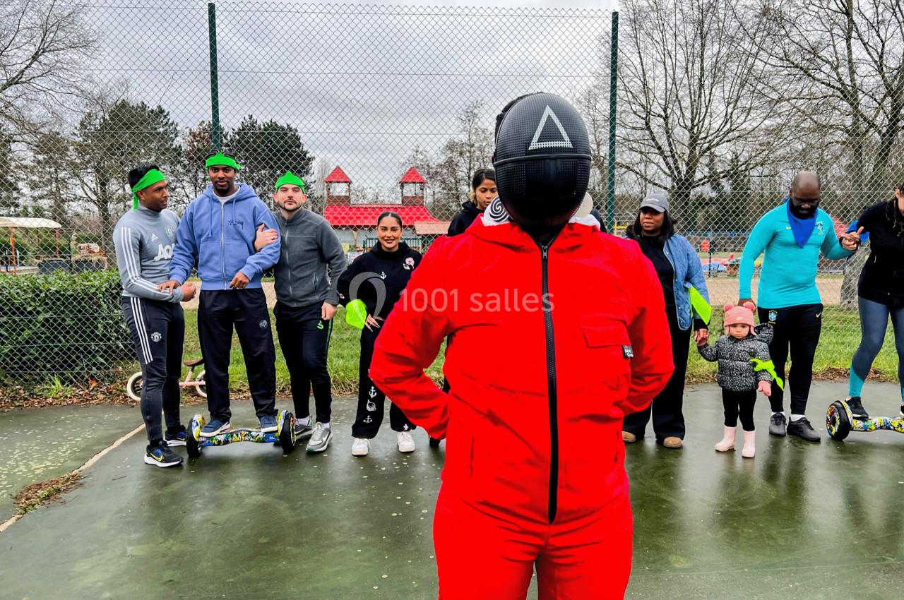 Une personne en combinaison rouge se tient devant un groupe d'adultes et d'enfants sur une aire extérieure.