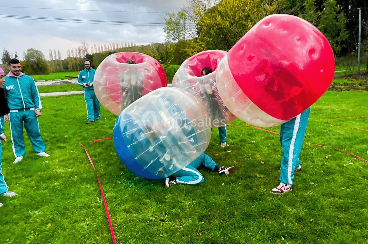 Des personnes vêtues de survêtements jouent au bubble football sur une pelouse verte par temps nuageux.