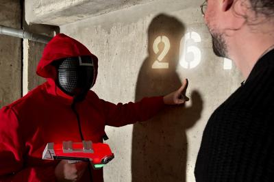 Une personne en combinaison rouge se tient devant un groupe d'adultes et d'enfants sur une aire extérieure.