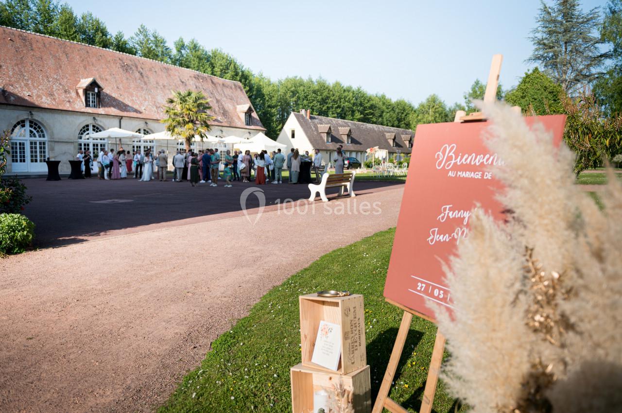 Groupe de personnes rassemblées devant un bâtiment en pierre, avec un panneau de bienvenue et des décorations au premier…