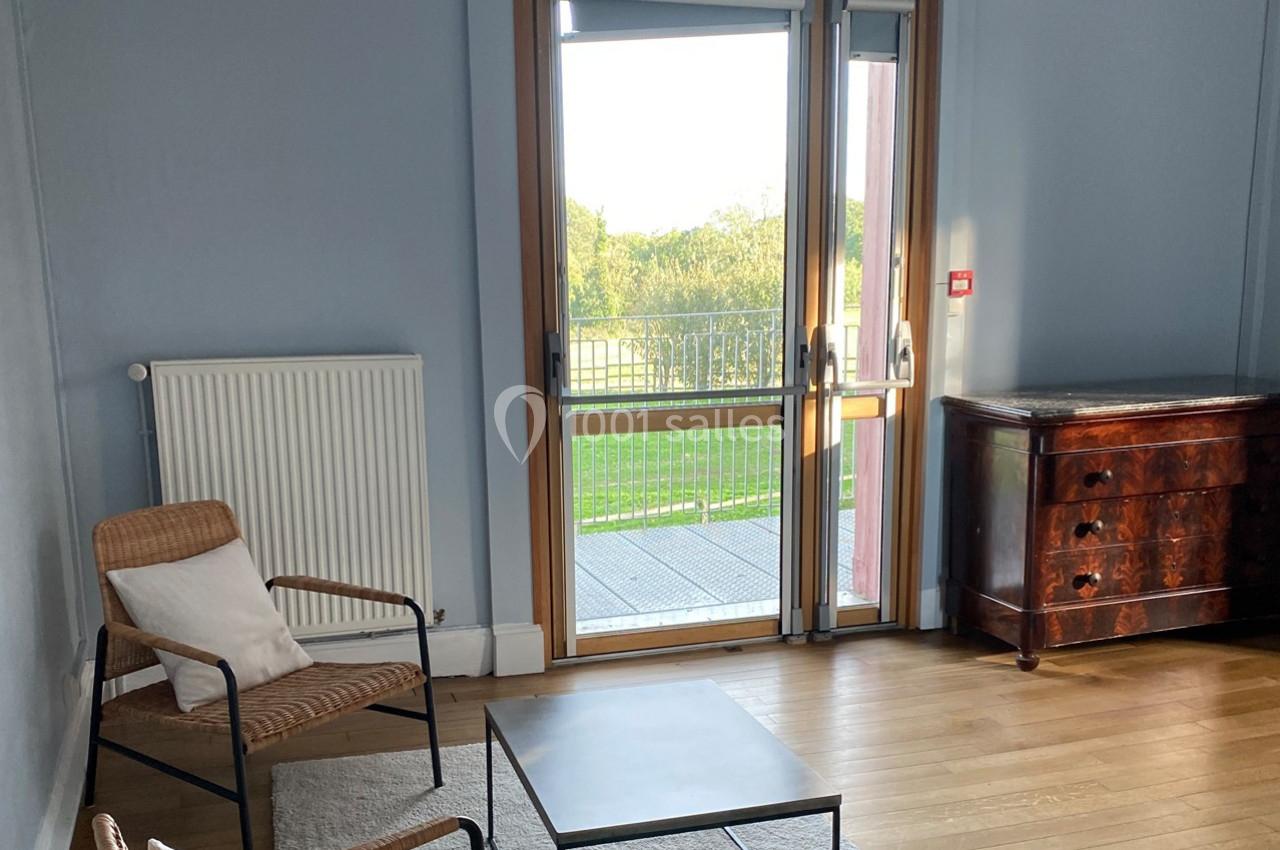 Deux fauteuils en osier, une table basse et une commode en bois dans une pièce lumineuse avec une porte-fenêtre donnant sur…
