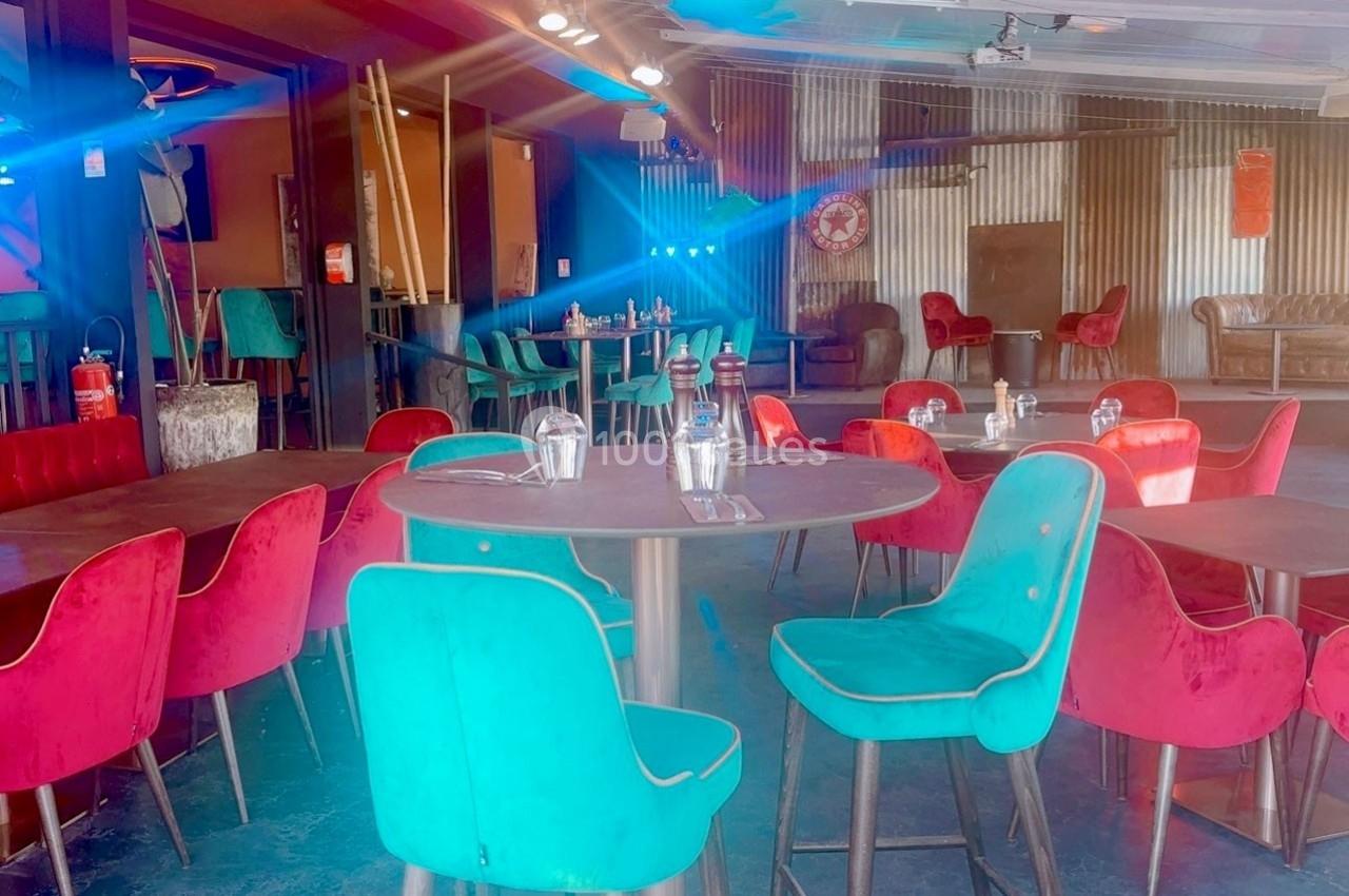 Salle de restaurant avec des tables dressées et des chaises colorées en velours rouge et turquoise.