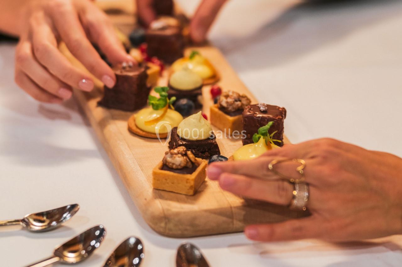 Des mains prennent des desserts variés disposés sur une planche en bois, avec des cuillères posées à côté.