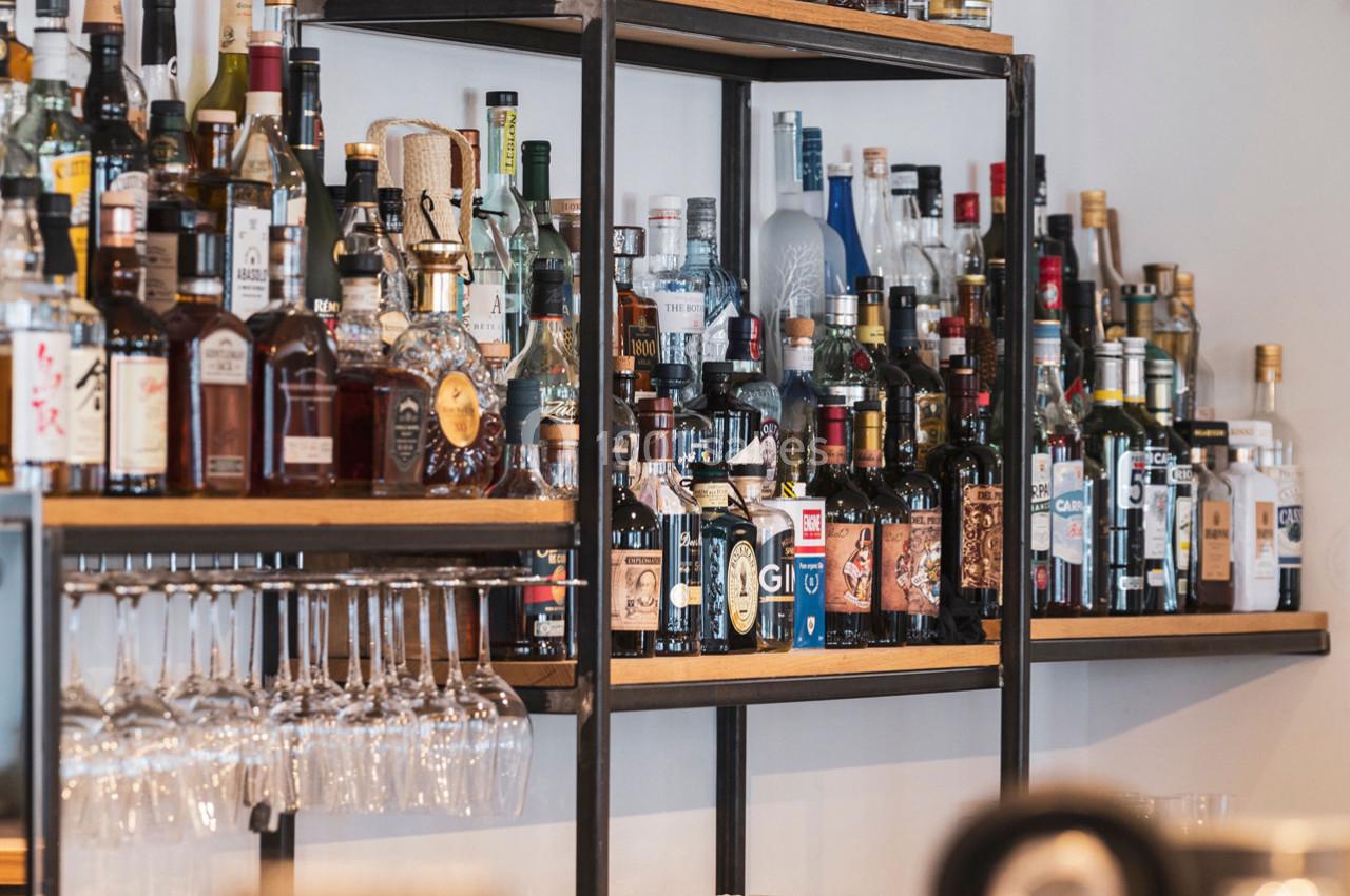 Étagères remplies de bouteilles d'alcool variées avec des verres suspendus en dessous dans un bar.