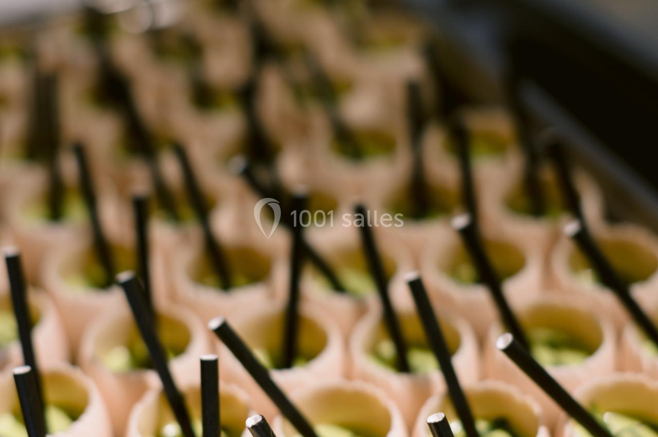 Des coquilles d'œufs remplies d'une mousse verte, chacune avec une paille noire, alignées sur un plateau.