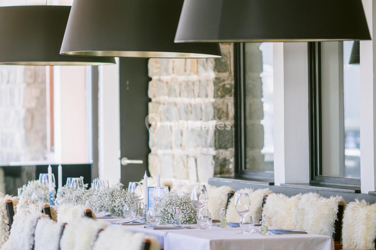 Salle de restaurant lumineuse avec tables dressées, chaises couvertes de fourrure et suspensions noires modernes.