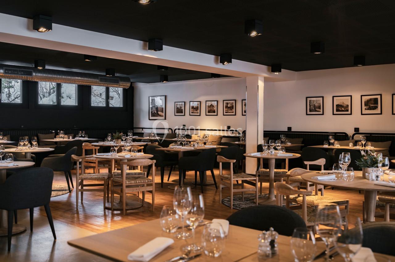 Salle de restaurant moderne avec tables dressées, chaises en bois et éclairage tamisé.