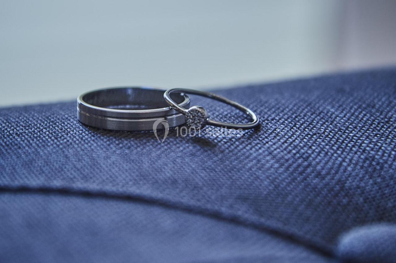 Deux anneaux, un en métal argenté et un avec un diamant, posés sur un tissu bleu texturé.