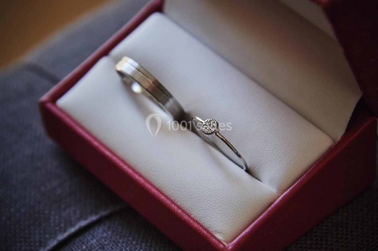 Deux alliances en métal, dont une ornée d'un diamant, présentées dans un écrin rouge ouvert.