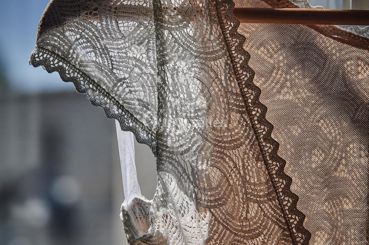 Dentelle beige et blanche d'un vêtement suspendu à un cintre, éclairée par la lumière naturelle près d'une fenêtre.