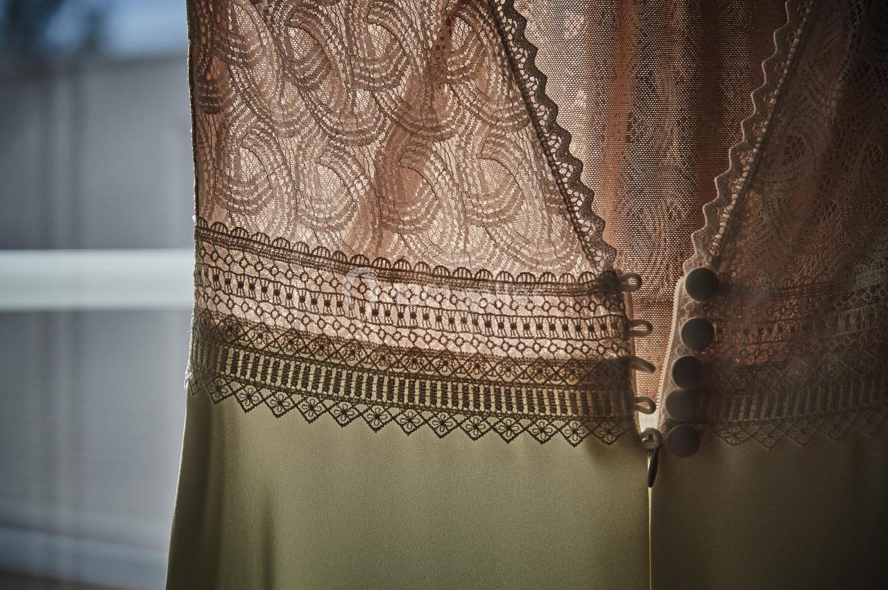 Dentelle beige délicate avec motifs complexes et boutons, éclairée par une lumière douce à travers une fenêtre.