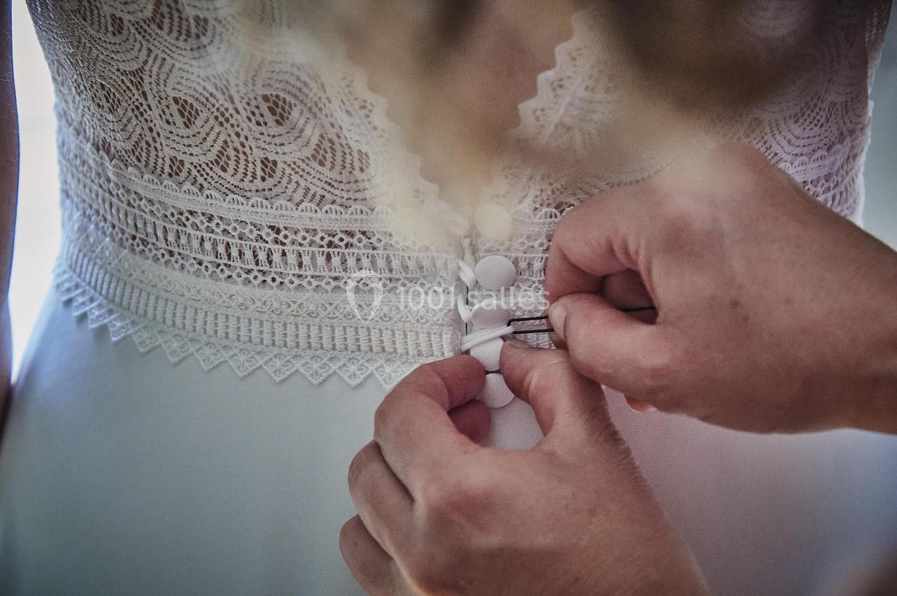 Main ajustant les boutons d'une robe de mariée en dentelle blanche.
