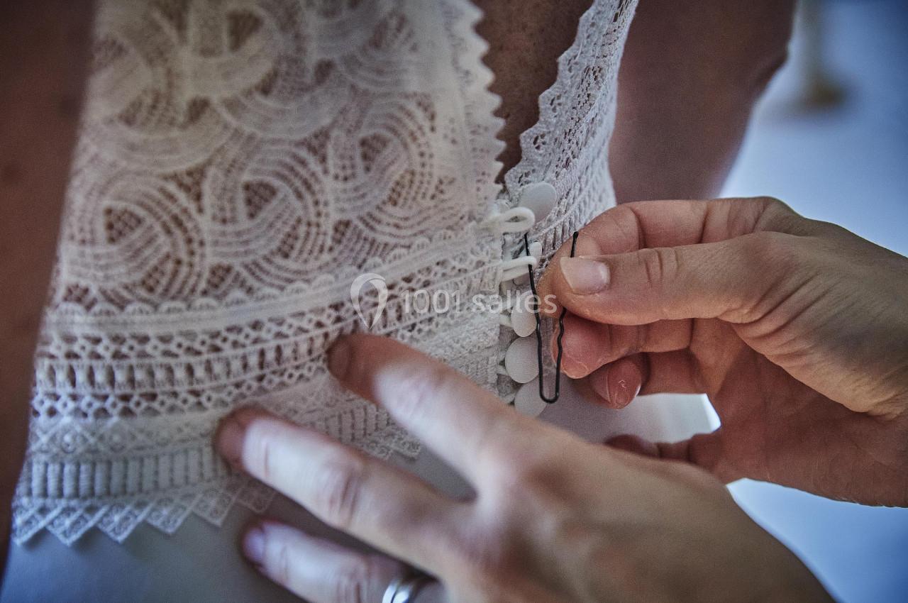 Main ajustant les boutons d'une robe en dentelle blanche.