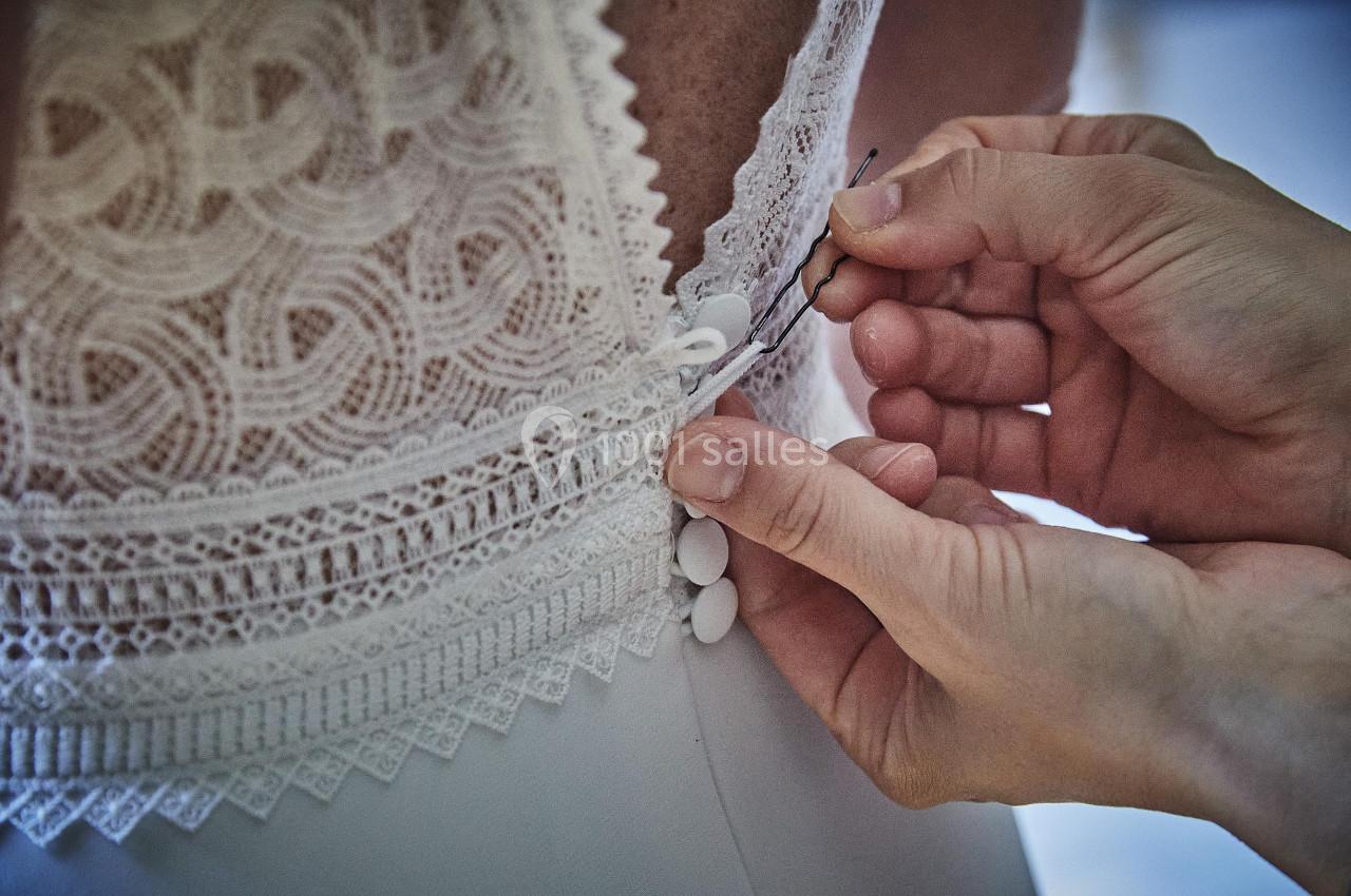 Main ajustant les boutons d'une robe en dentelle blanche dans le dos.