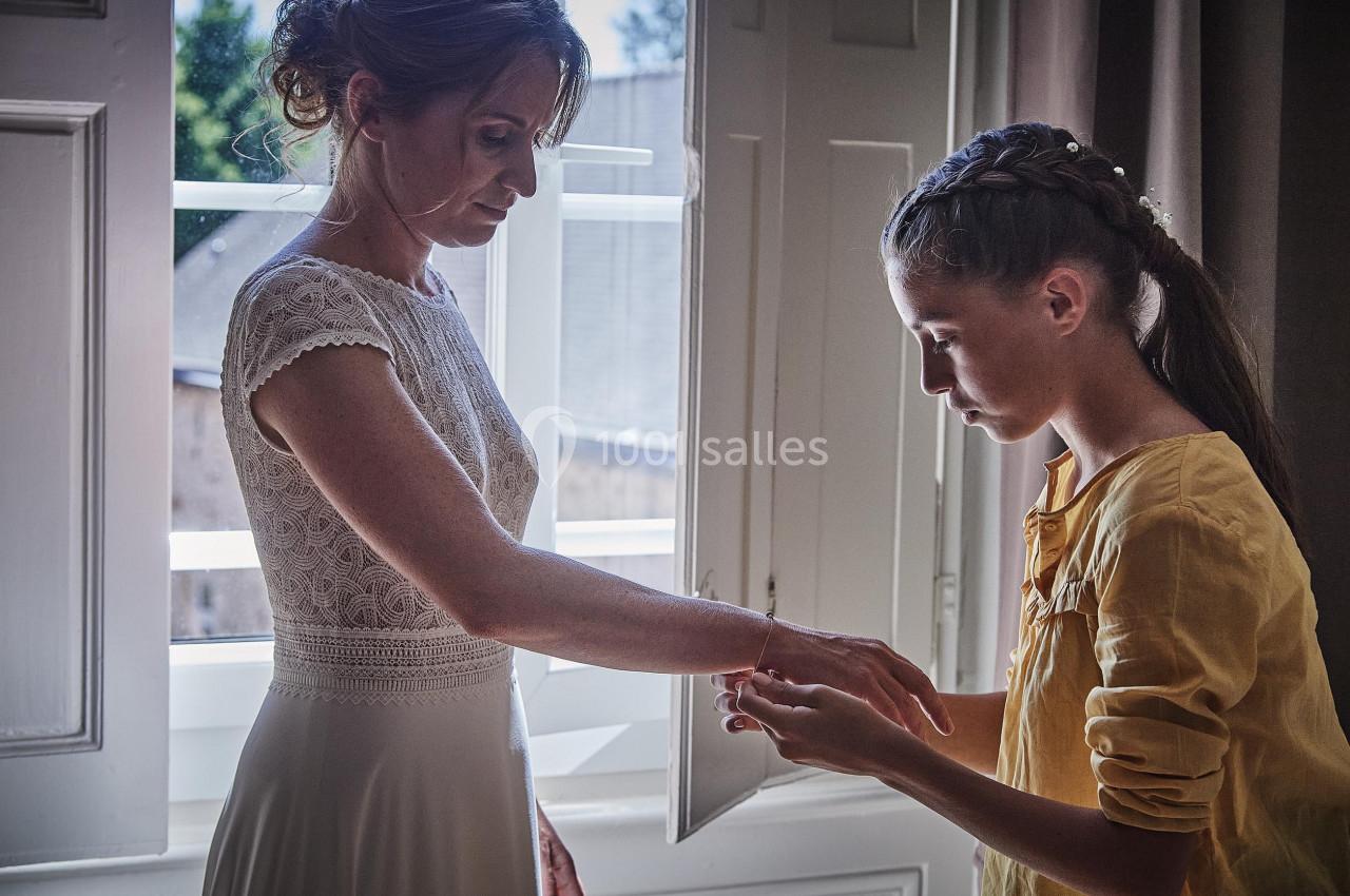 Une femme en robe blanche et une jeune fille en chemisier jaune échangent un moment près d'une fenêtre ouverte.
